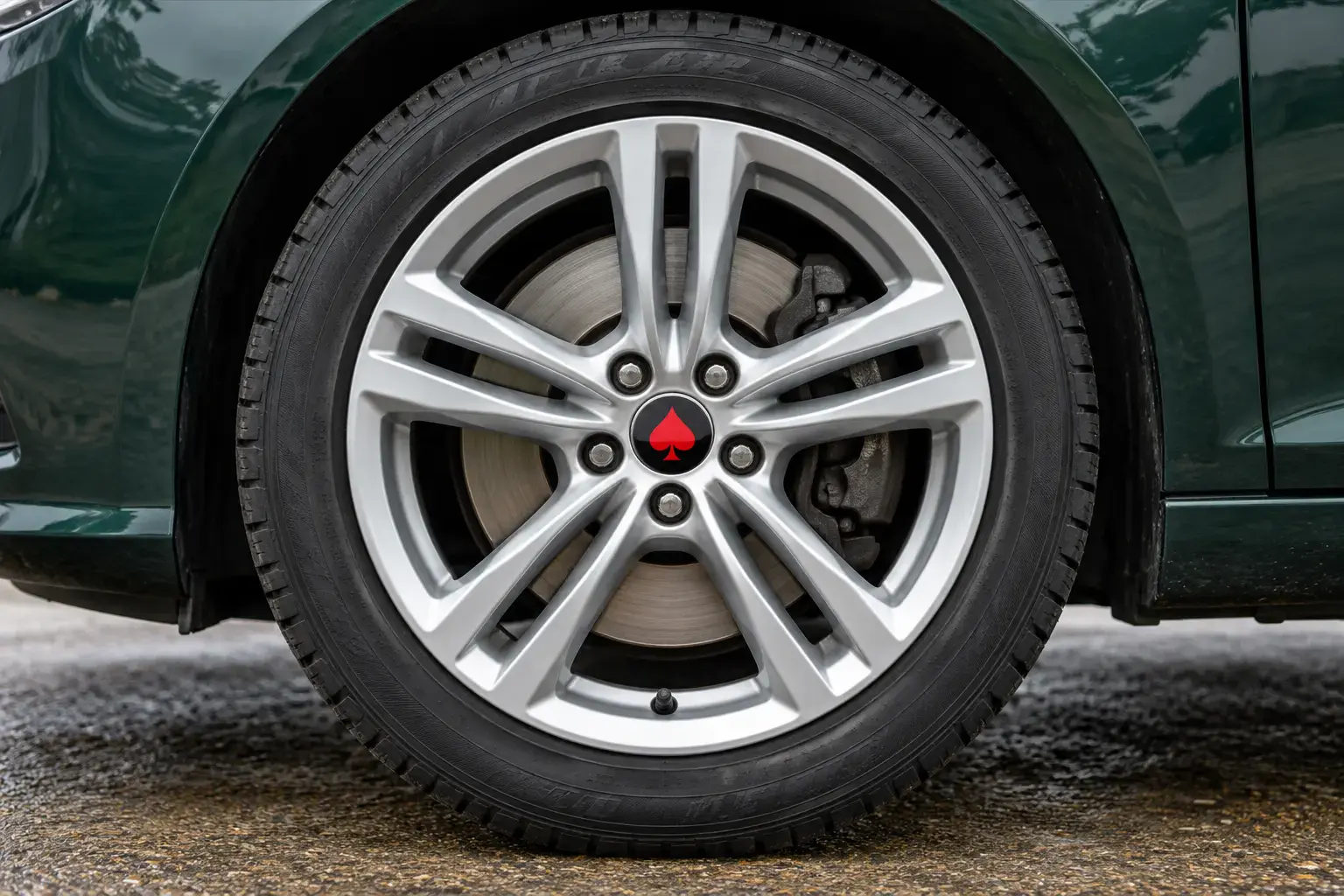 Illustrative silver alloy wheel with a renewed finish on a dark green car